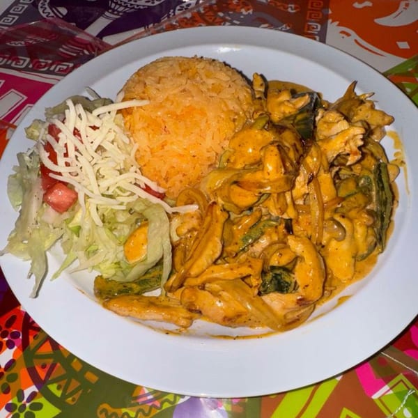 La Poblanita's chicken fajitas with rice, lettuce, tomatoes, and shredded cheese on a white plate.