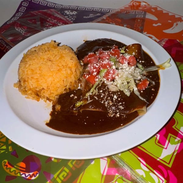 La Poblanita's enchiladas with rich mole sauce, rice, and fresh toppings on a colorful placemat.