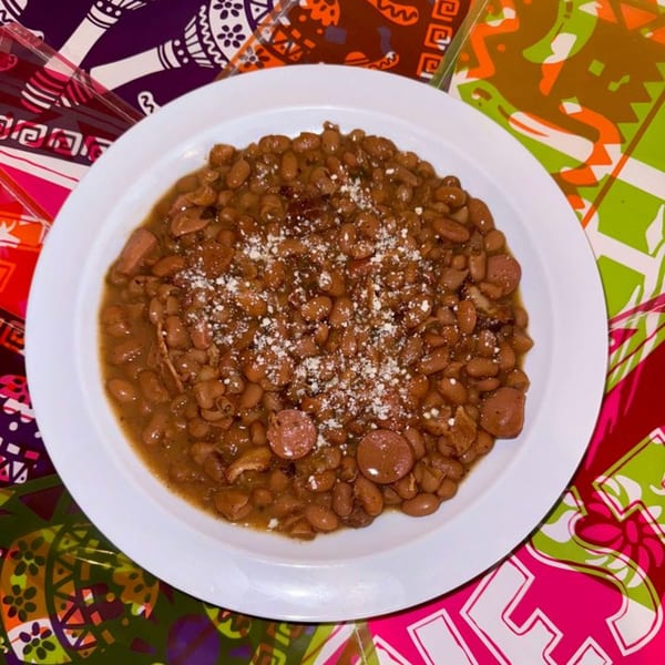 A white plate of La Poblanita's charro beans with sliced hot dogs and cotija cheese.