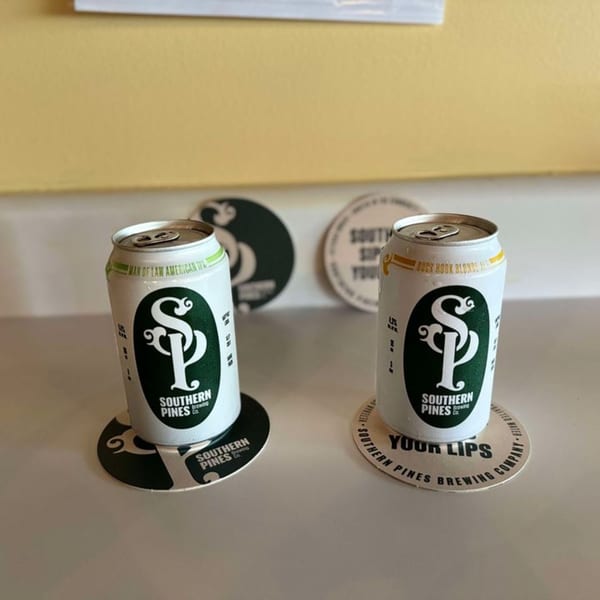 Two Southern Pines Brewing Company beer cans on coasters, one "Man of Law American IPA" and one "Duck Hook Blonde Ale".
